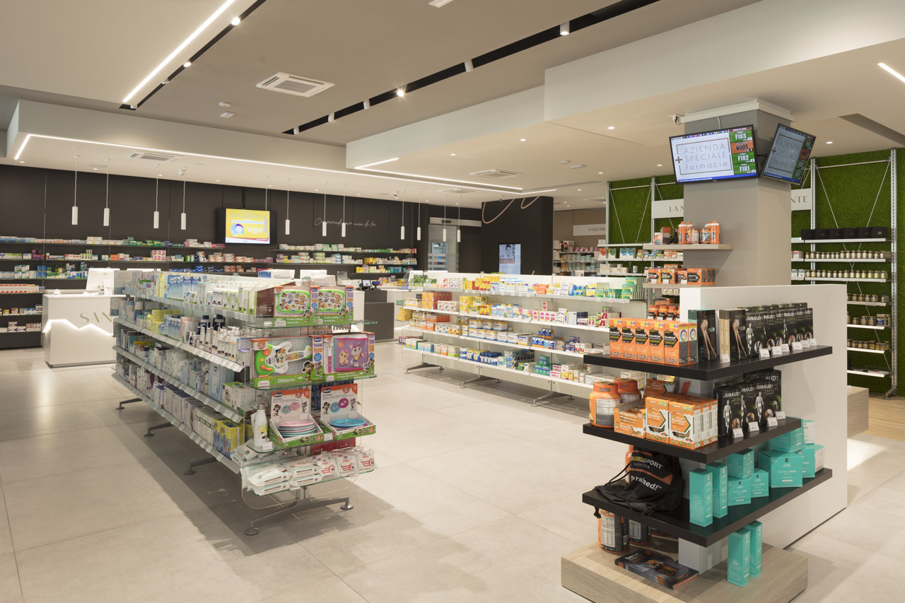 interno di una farmacia moderna, con bancone, schermo per la gestione dei clienti ed espositori modulari.